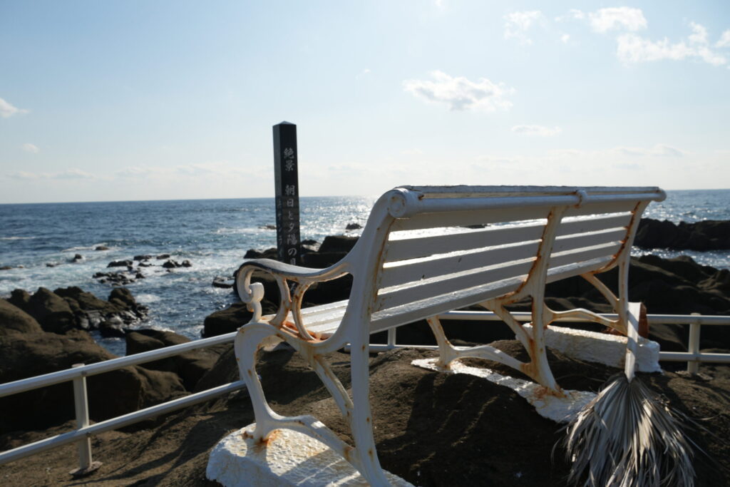 野崎島灯台にある崖の上のベンチの写真。ベンチの目の前には「朝日と夕陽が見えるベンチ」とある。東西に広がる水平線と海風が気持ちよい