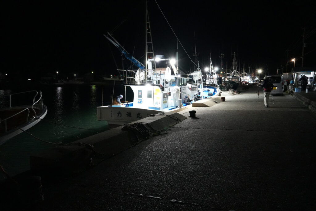 大原漁港で出向を待つ釣り船と釣り客。夜明け前の海と釣り船の灯のコントラスト